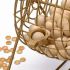 Boule numérotée en bois sortant d'une cage de loto en métal doré, avec des jetons en bois posés sur une surface blanche.