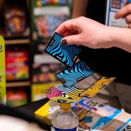 Main d’un adulte posant une carte bleue sur une structure en équilibre au-dessus d’une bouteille.