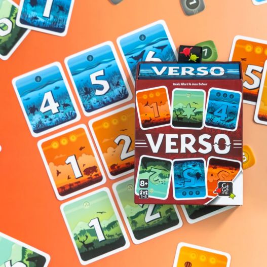 Boîte du jeu Verso au centre d’un plateau de jeu multicolore avec des cartes rangées autour.