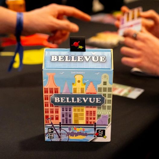 Boîte du jeu Bellevue sur une table de jeu pendant une partie avec des joueurs autour.
