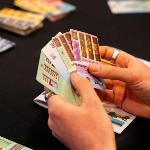 Main d’un joueur tenant plusieurs cartes du jeu Bellevue représentant des façades de maisons.