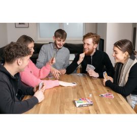 Cinq amis autour d'une table en train de jouer à Papayoo, tous souriants et concentrés sur leurs cartes.