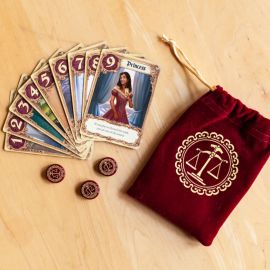 Cartes du jeu Love Letter étalées autour d’une pochette en velours rouge brodée du logo de la balance.