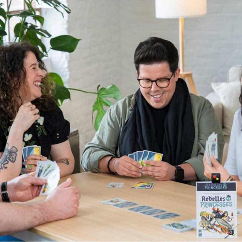Groupe d'adultes jouant au jeu Rebelles Princesses autour d'une table, ambiance joyeuse.