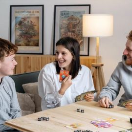 Trois joueurs souriants autour d'une table pendant une partie de Wazabi, cartes en main.