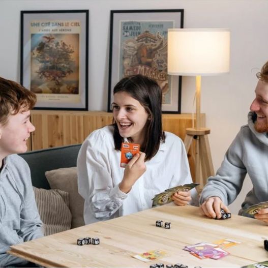 Trois joueurs souriants autour d'une table pendant une partie de Wazabi, cartes en main.