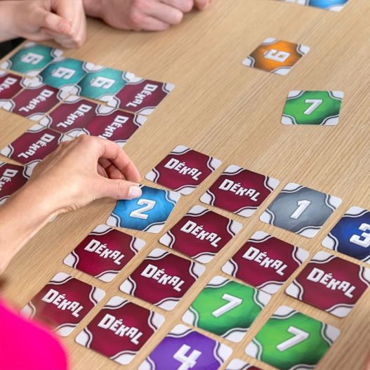 Joueurs retournant des cartes DÉKAL numérotées lors d'une partie sur une table en bois.
