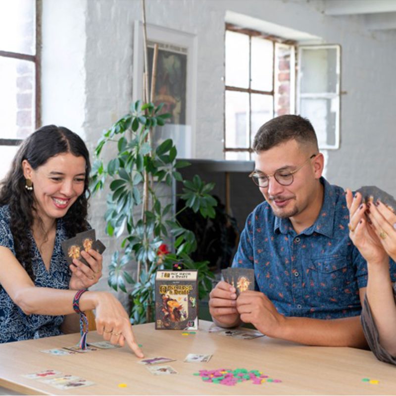 Groupe de quatre personnes concentrées et souriantes jouant à Once Upon a Draft, boîte du jeu visible au centre de la table.