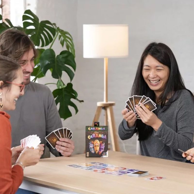 Scène conviviale où des joueurs rient tout en jouant à Cabanga à une table.