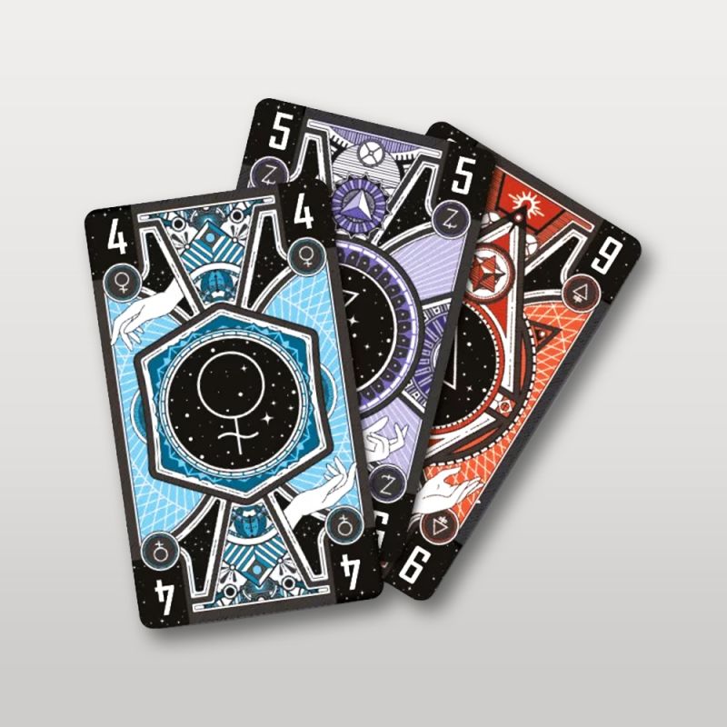 Trois cartes du jeu Aurum aux motifs alchimiques et couleurs bleu, violet et rouge.