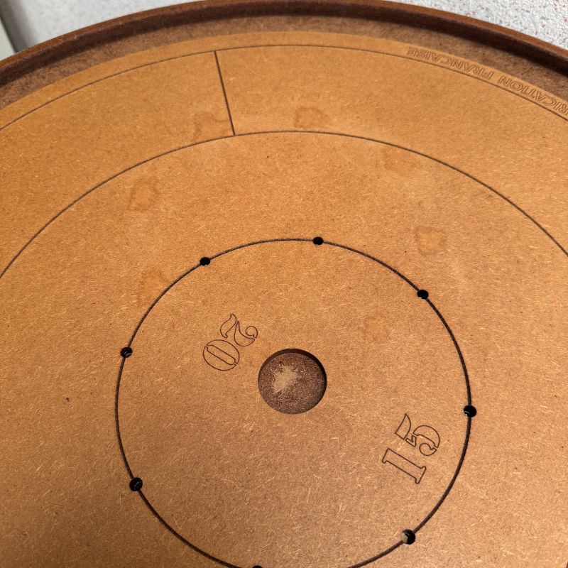 gros plan sur des marques sombres au centre d'un plateau de crokinole en bois clair