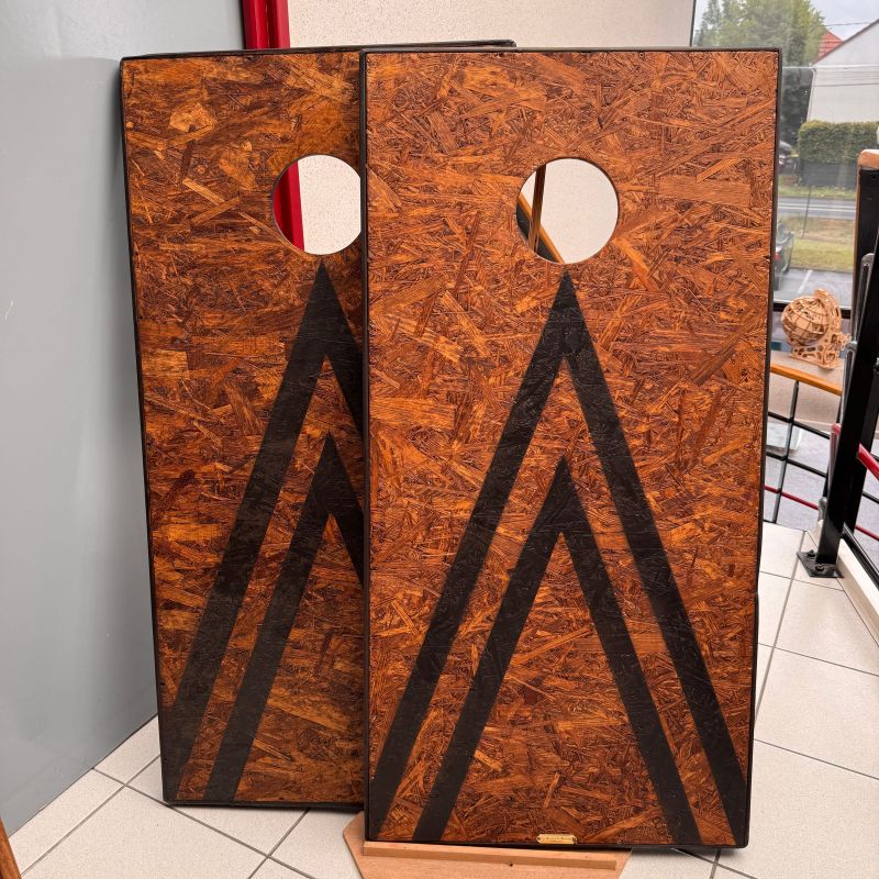 Les deux plateaux du cornhole posés debout côte à côte, avec leur trou de visée et leur motif de chevrons