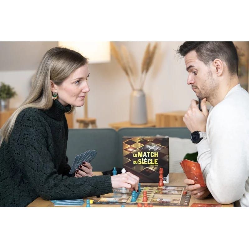Deux joueurs assis face à face, cartes en main, autour du plateau posé sur une table basse