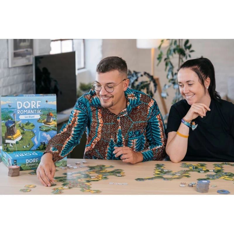 Deux joueurs installés à table avec des tuiles hexagonales déployées et la boîte du jeu ouverte à côté