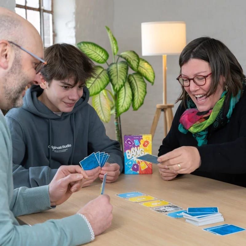 Trois joueurs souriants autour d'une table, cartes bleues en main pendant une partie de Bango