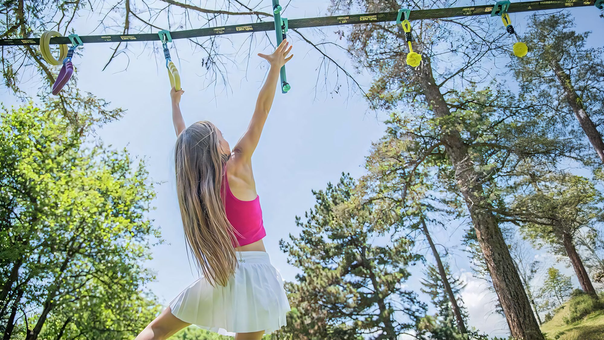 Enfant souriant suspendu à la ligne d'aventure Ninja Trelines en extérieur.