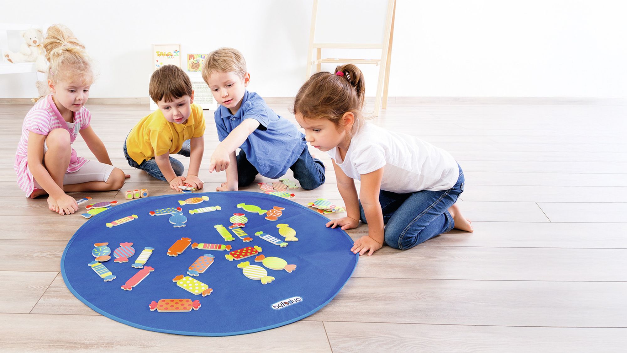 Groupe d'enfants jouant au jeu éducatif avec des bonbons colorés sur un tapis bleu.