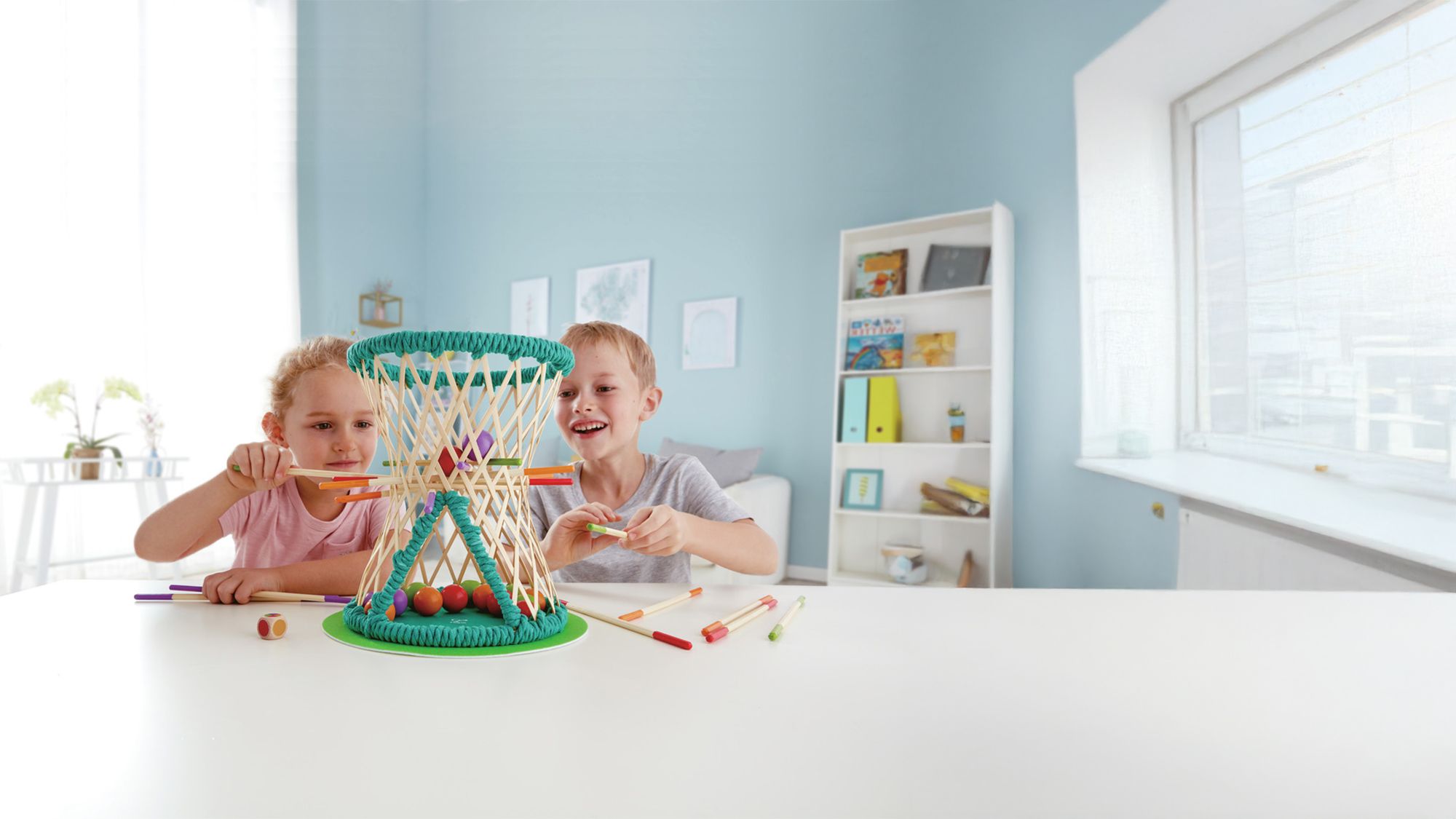 Deux enfants jouant avec un panier de jeu dans une pièce lumineuse, insérant des bâtonnets colorés.