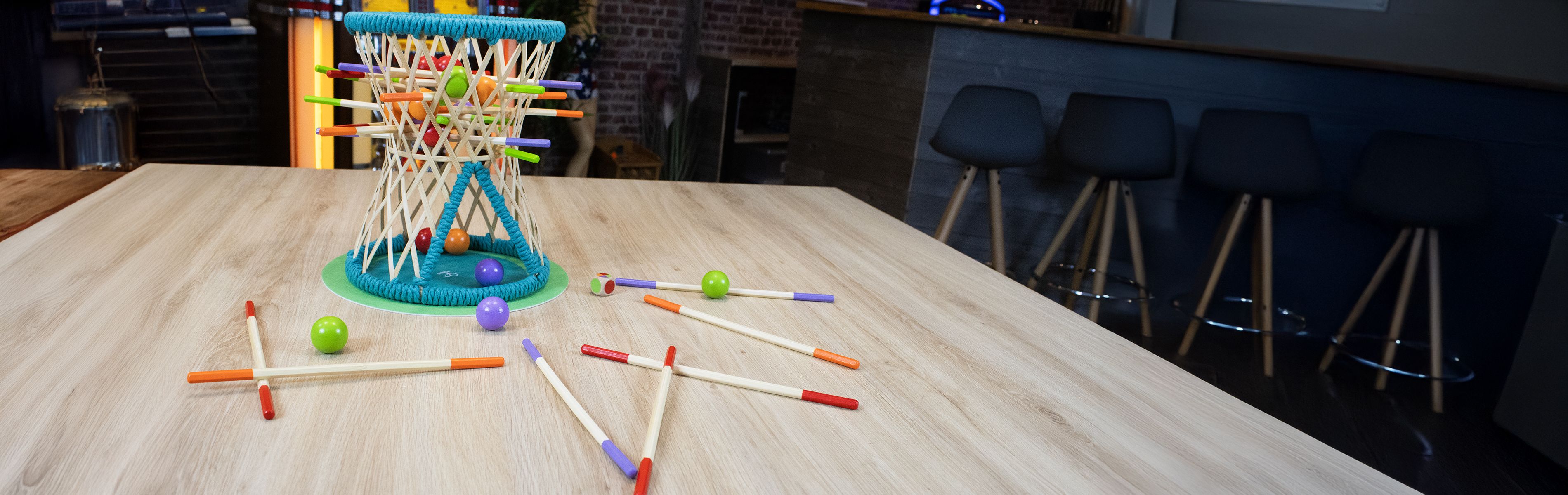 Vue en gros plan d'un jeu avec des bâtonnets colorés insérés dans un panier en forme de roue, avec des boules colorées sur la table.