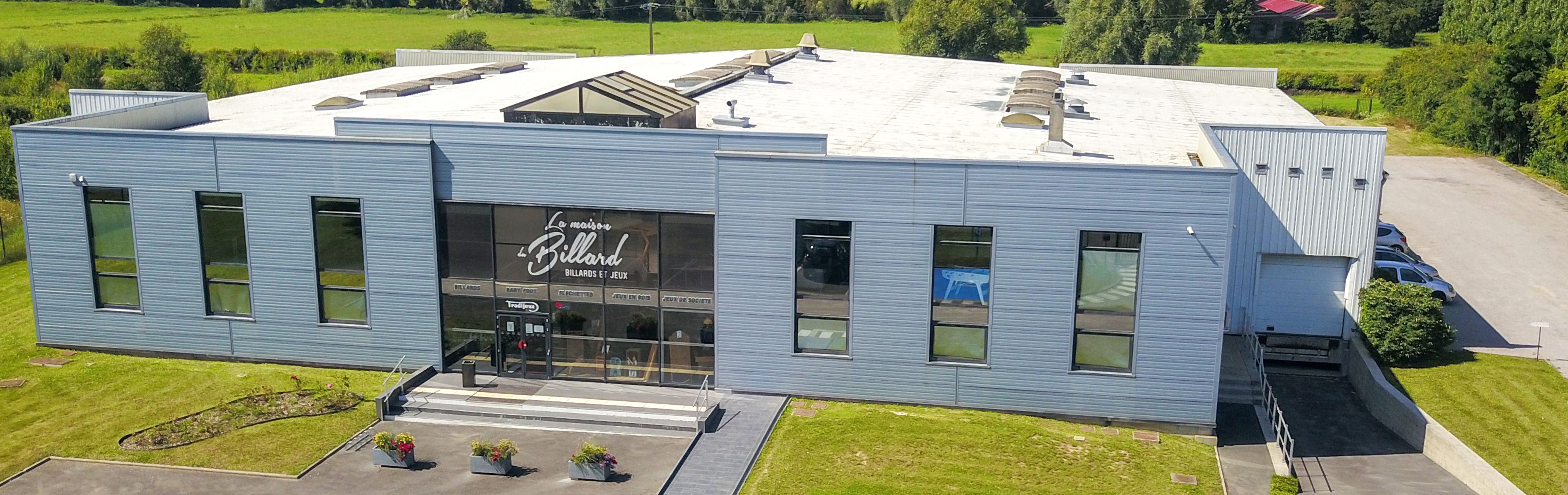 Vue d'un bâtiment industriel avec un parking à l'extérieur et un logo visible sur la vitrine.